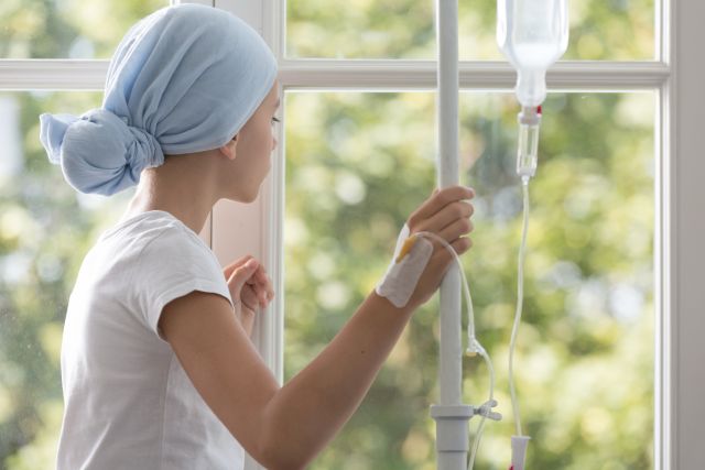 Krankes Kind mit Infusion und blauem Kopftuch während der Behandlung im Krankenhaus