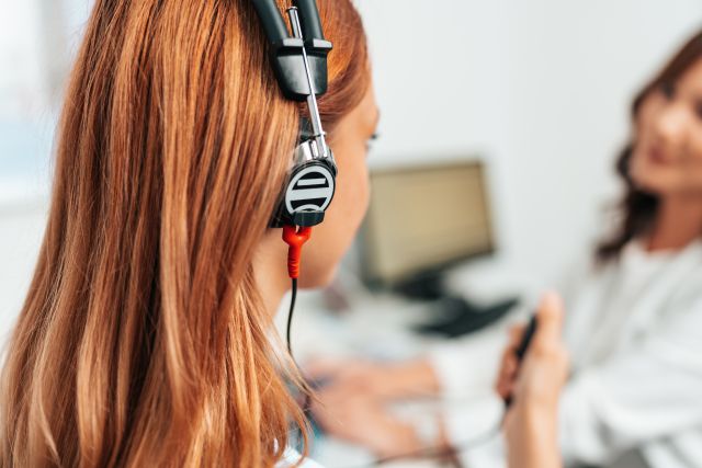 Audiologe führt Impedanzaudiometrie oder Diagnose von Hörstörungen durch. Eine schöne rothaarige erwachsene Frau lässt sich in einer Hörklinik einem Hörtest unterziehen. Nahaufnahme.