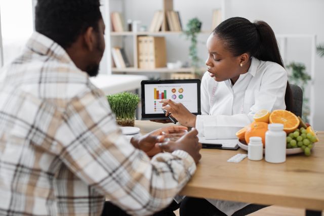 Ernährungsberater analysiert Daten auf Tablet mit Patient in der Klinik