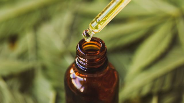 Tropfen pharmazeutisches CBD-Öl auf Hanfbasis mit verschwommenem Hintergrund aus Cannabis-Marihuana-Blättern