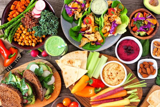 Bunte vegane Gerichte mit frischem Gemüse, Hummus, Salatwraps und grünem Smoothie auf einem Holztisch