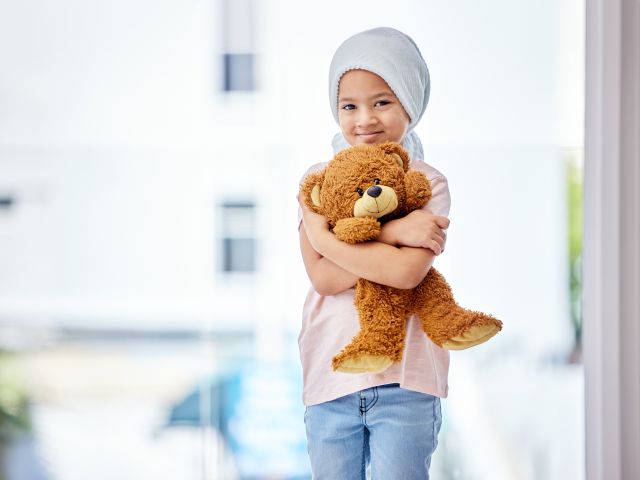 Kleines Kind mit Krebs umarmt einen Teddybär