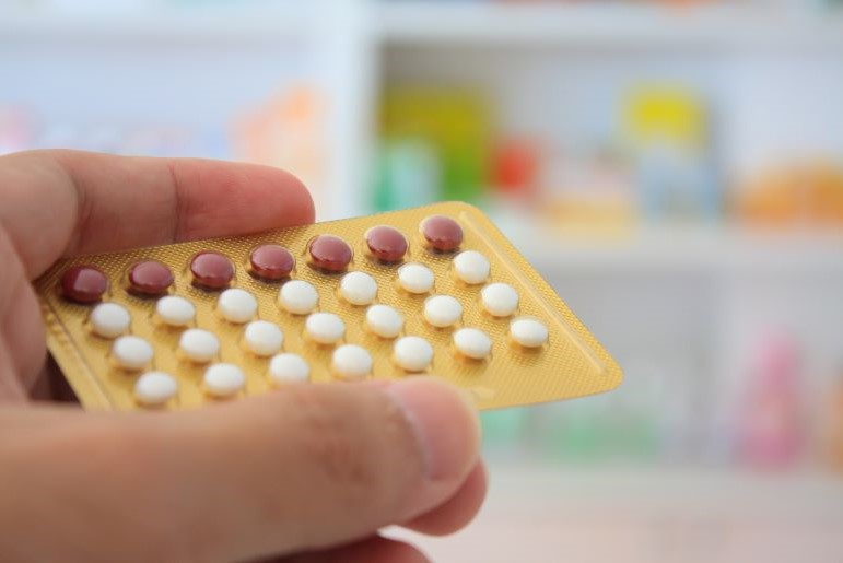 Hand hält Blisterpackung mit Antibabypillen. Braune und weiße Tabletten auf gelbem Hintergrund.