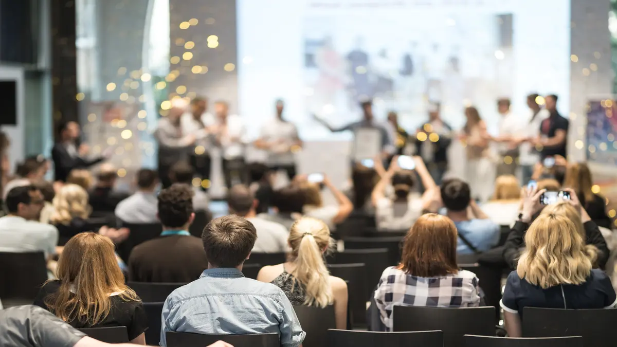 Ein Konferenzraum mit Publikum, das einer Präsentation auf der Bühne folgt. Ideal für Themen wie Events, Konferenzen oder Networking.