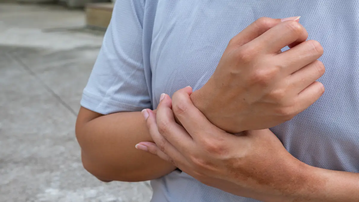 Ein Mann hält sich sein Handgelenk und scheint unter Schmerzen zu leiden.