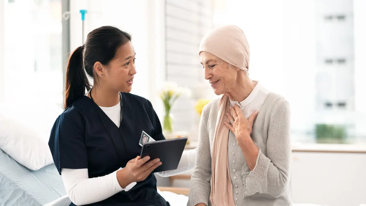 Eine Krankenschwester nutzt ein Tablet, um eine ältere Krebspatientin im Krankenhaus zu beraten.