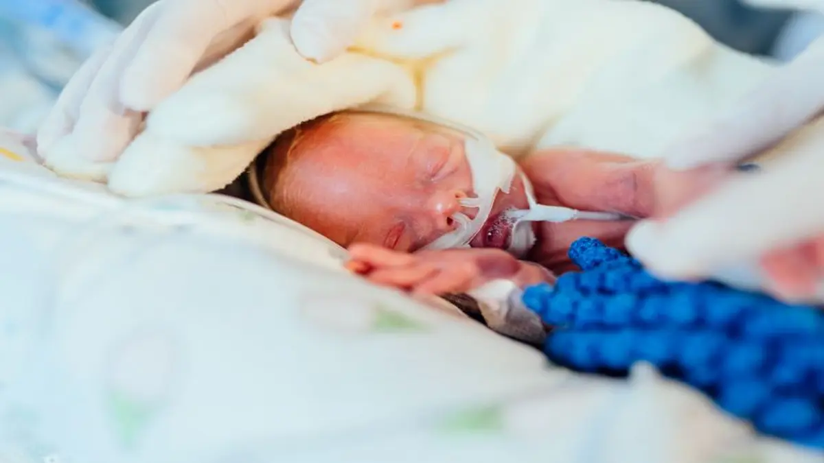 Frühgeborenes Baby auf der Intensivstation, liebevoll umsorgt mit Decke und Beatmungsschlauch.