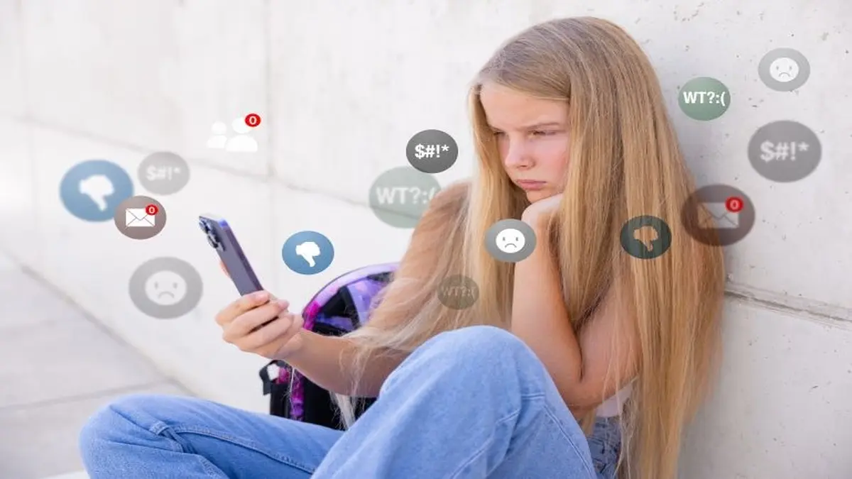 Das Bild zeigt ein jugendliches Mädchen in der Pubertät, das am Smartphone sitzt; negative Social Media Kommentare und Icons wirken auf ihre Selbstwahrnehmung.