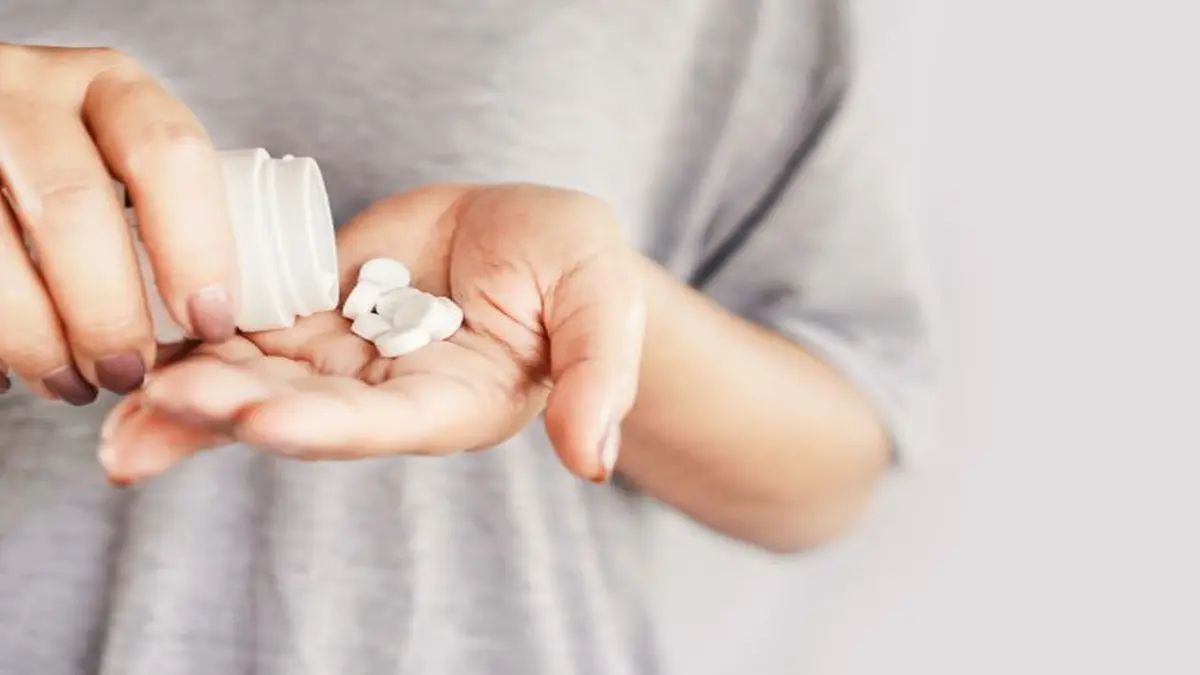 Eine Hand hält weiße Tabletten aus einer geöffneten Dose.