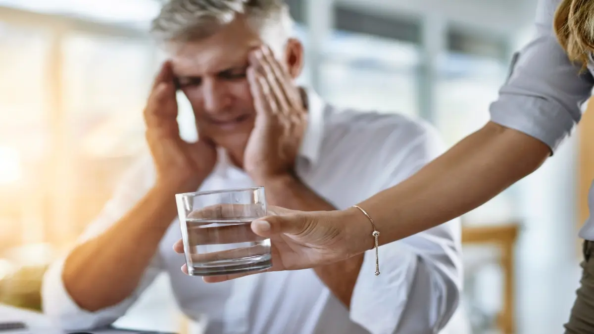 Mann mit Migräne, dem Wasser gereicht wird