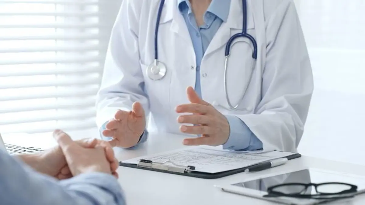 Arzt im Gespräch mit einem Patienten am Schreibtisch, Fokus auf Hände und Unterlagen
