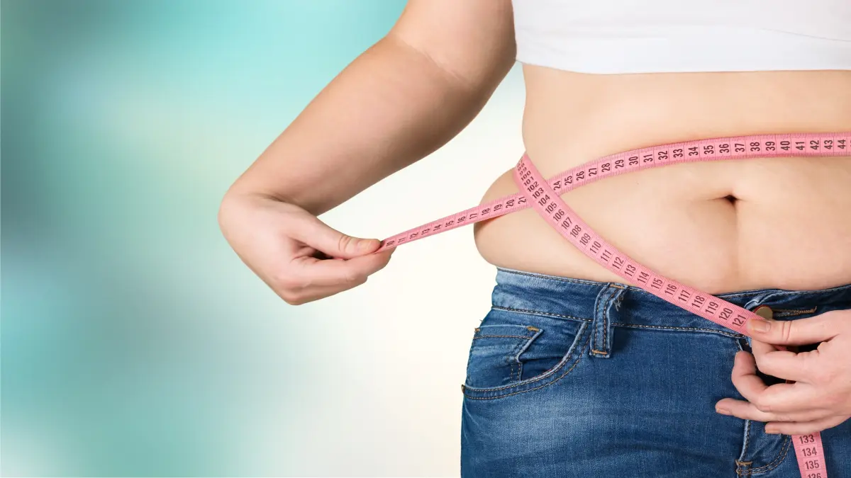 Frau misst ihren Bauchumfang mit einem pinken Maßband, symbolisiert Gewichtsabnahme und Gesundheit.