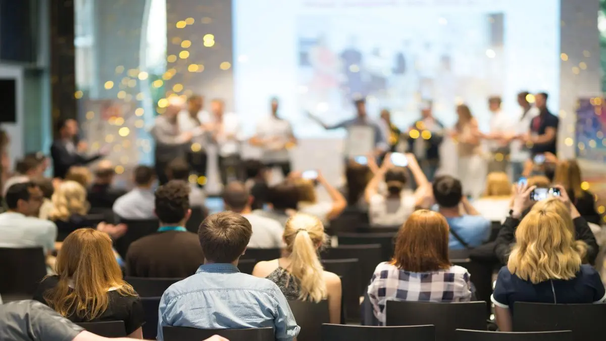 Publikum bei einer Konferenz, das aufmerksam einer Gruppenpräsentation auf einer Bühne folgt