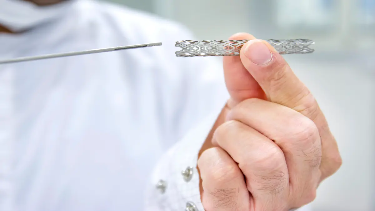 Hand hält einen medizinischen Stent, daneben ein Einführungsinstrument, Nahaufnahme