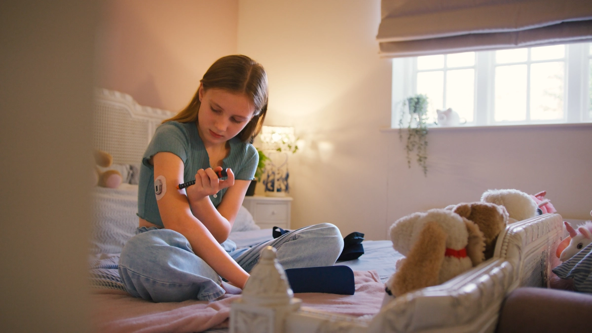 junges Mädchen mit Diabetes-Equipment sitzt auf ihrem Bett im Kinderzimmer