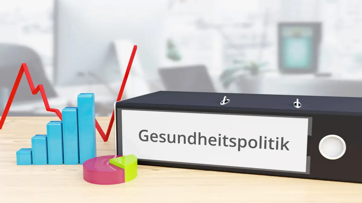 Ein schwarzer Ordner mit der Aufschrift "Gesundheitspolitik" liegt auf einem Schreibtisch.