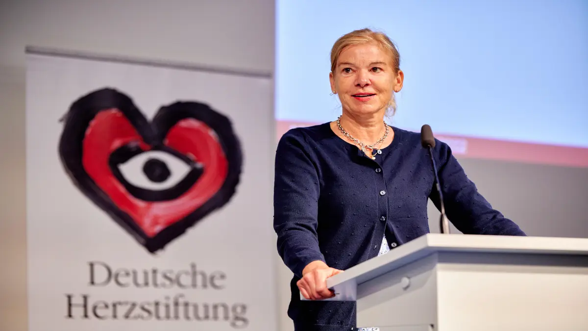 Frau am Rednerpult vor einem Banner der Deutschen Herzstiftung mit Herz-Logo