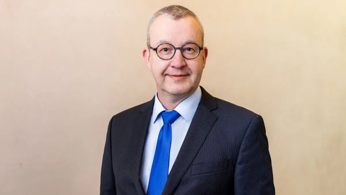 Portrait von Dr. Axel Belusa, Präsident des BvDU, in einem dunklen Anzug mit blauer Krawatte vor neutralem Hintergrund.