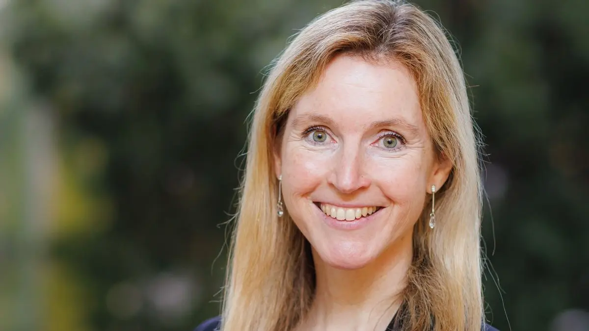 Business-Portrait von Dr. Martina Schmidhuber vor einem natürlichen Hintergrund, mit lila Oberteil und schwarzem Blazer.