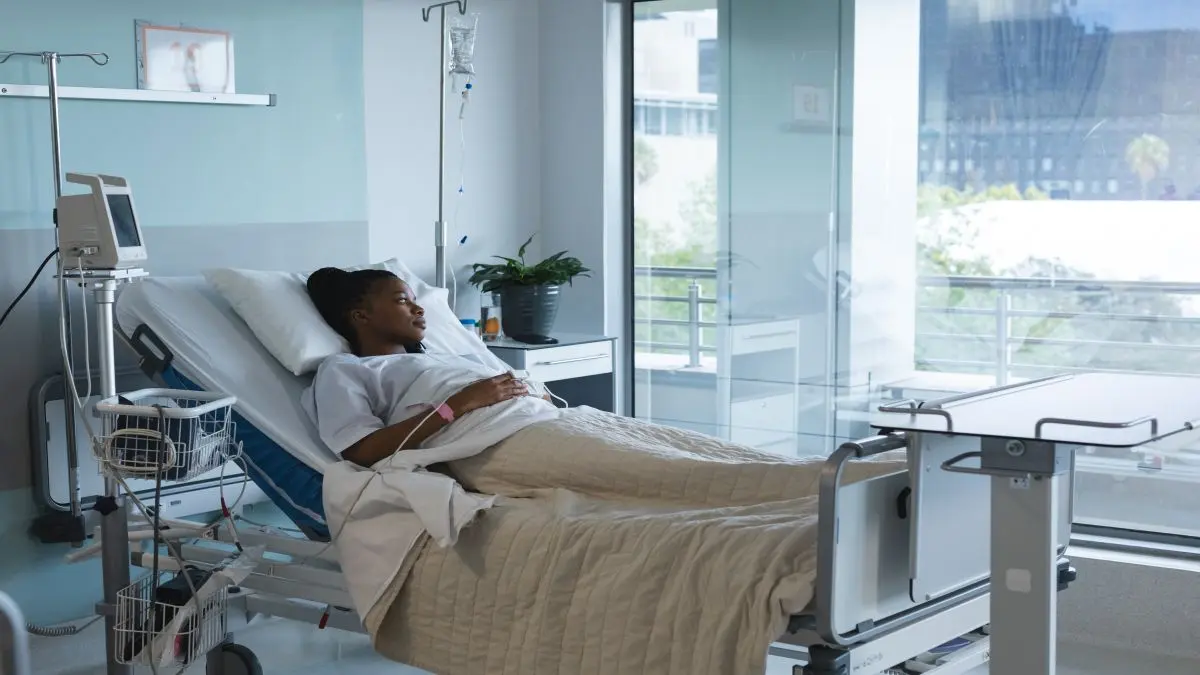 Patientin im Krankenhausbett in hellem Zimmer mit Infusion und medizinischem Gerät