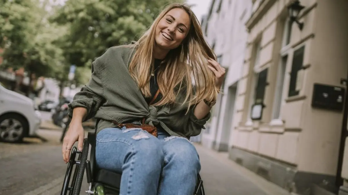 Eine Frau im Rollstuhl bewegt sich selbstständig durch eine urbane Umgebung, symbolisiert Selbstbestimmung und Mobilität.
