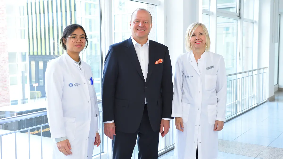 Dr. Sicilia Subagia, Dr. Wolfgang Walter und Prof. Dr. Ioanna Gouni-Berthold stehen in einem hellen Flur der Uniklinik Köln.