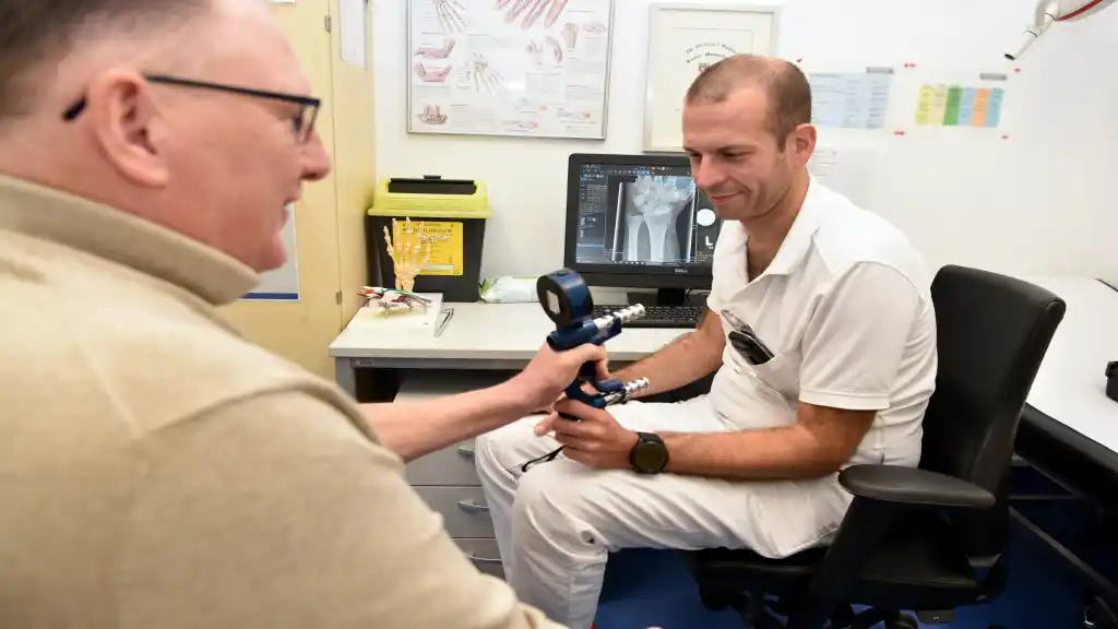 Dr. Patrick Harenberg führt mit dem Patienten eine Kraftmessung an der operierten Hand durch.