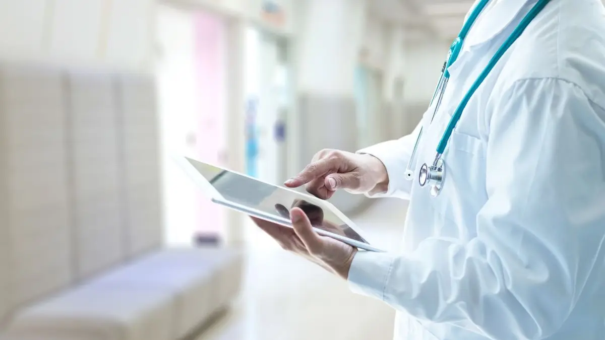 Arzt mit Stethoskop nutzt Tablet in moderner Klinik – Digitalisierung im Gesundheitswesen