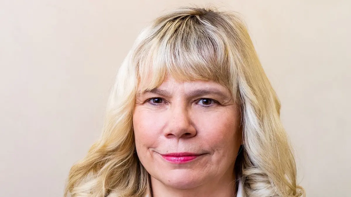 Portrait von Catrin Steiniger in einem dunklen Blazer und weißer Bluse vor neutralem Hintergrund.