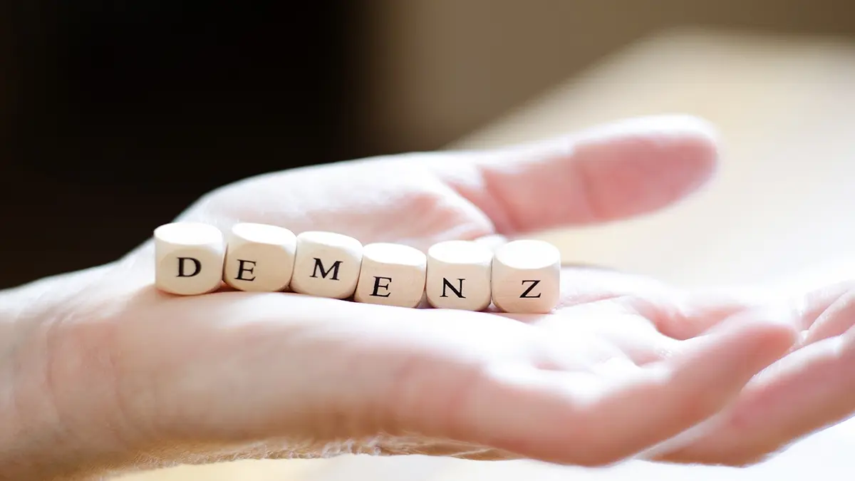 Holzbuchstaben mit der Aufschrift "Demenz" auf einer offenen Hand.