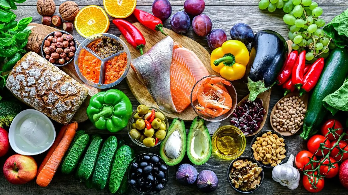 Frische und gesunde Lebensmittel wie Obst, Gemüse, Fisch, Nüsse und Oliven auf einem Holztisch.