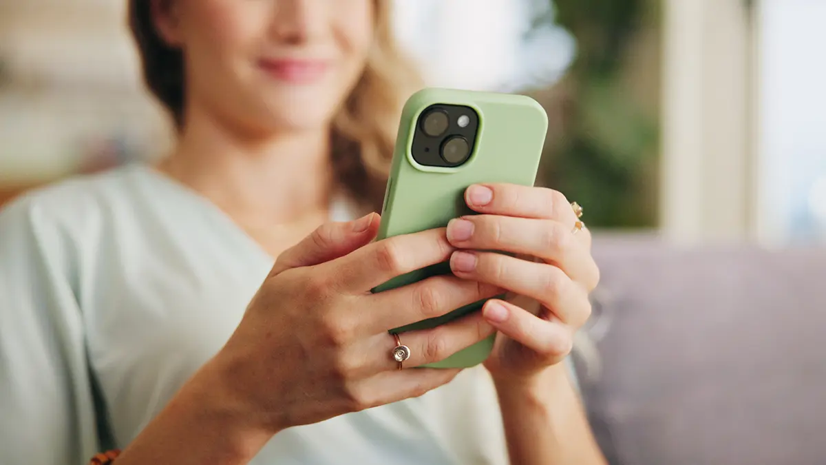 Person hält ein Smartphone mit grünem Case, möglicherweise zur Nutzung einer App für Inkontinenz-Management oder Blasengesundheit.