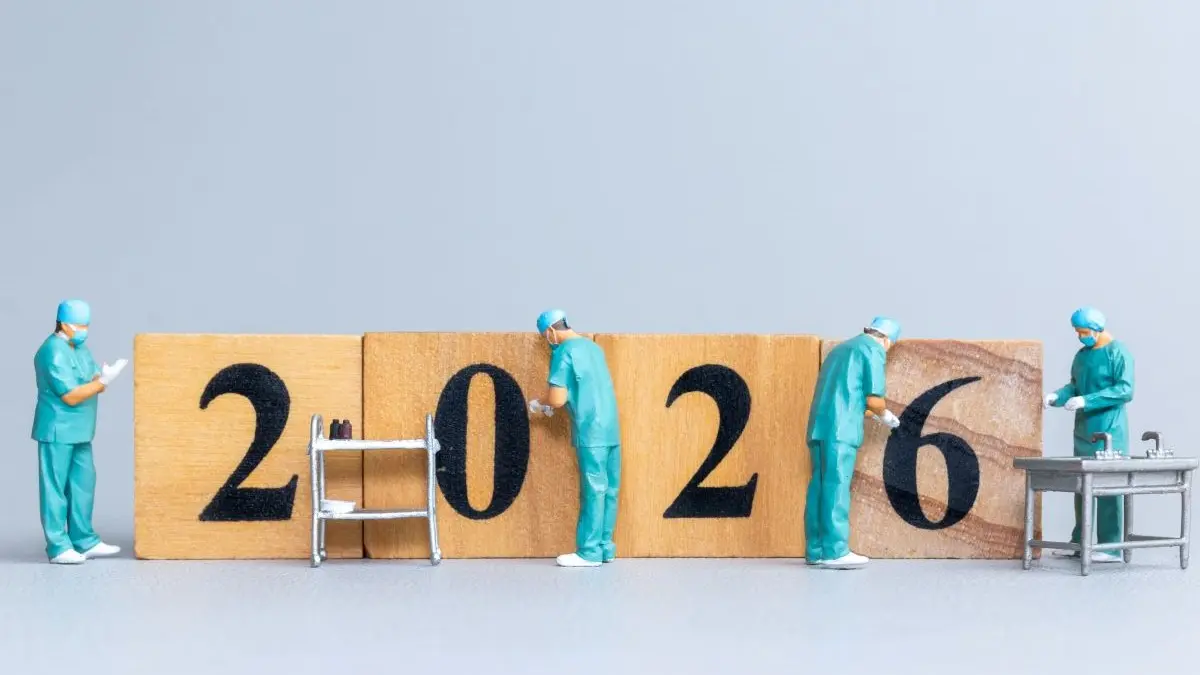 Miniatur-Chirurgen arbeiten an Holzblöcken mit der Zahl 2026, symbolisiert Fortschritte in der Medizin.
