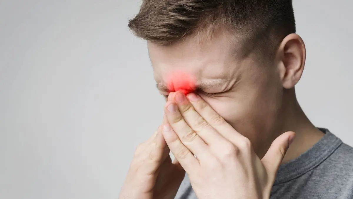 Person hält sich die Nase, symbolisiert Beschwerden oder Schmerzen im Nasenbereich.