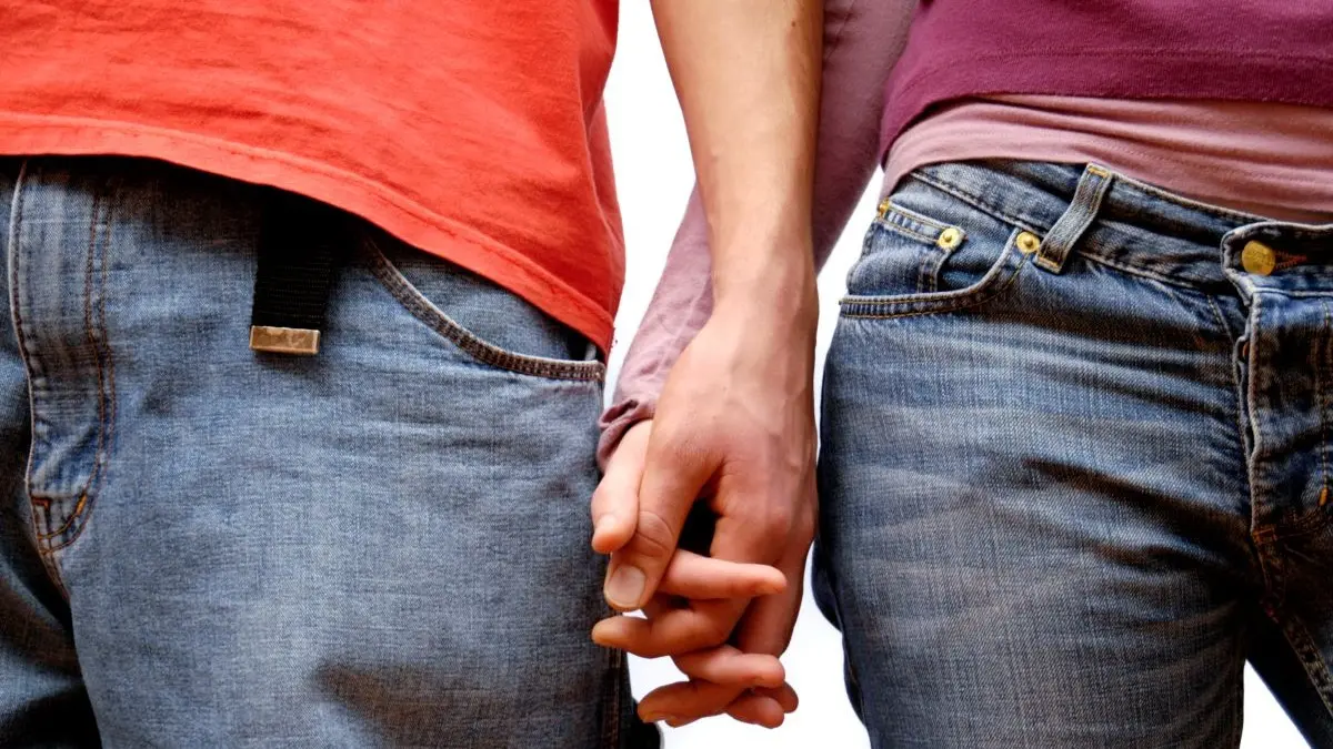Zwei Personen halten Händchen und tragen Jeans – Symbol für Partnerschaft und Zusammenhalt