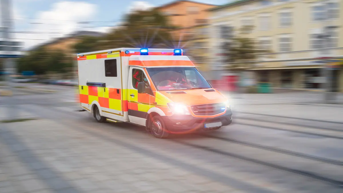Krankenwagen im Einsatz mit eingeschaltetem Blaulicht auf einer städtischen Straße.