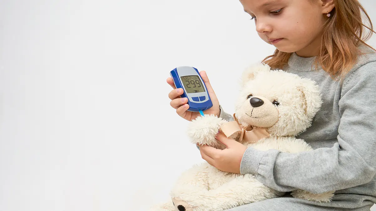 Kind hält ein Blutzuckermessgerät und einen Teddybären, symbolisch für Typ-1-Diabetes.