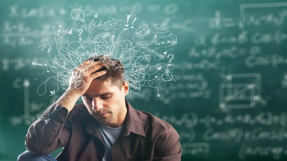 Ein junger Mann steht nachdenklich und gestresst vor einer Tafel voller mathematischer Formeln und Gleichungen.