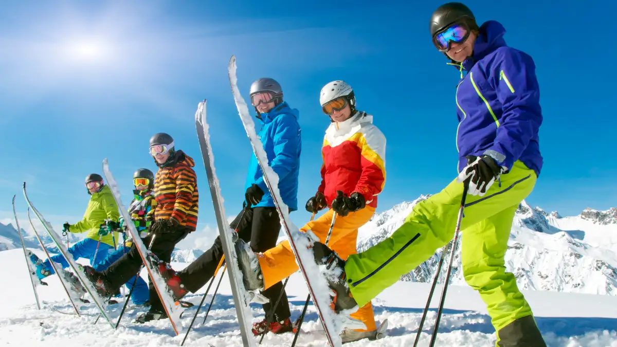 Sechs Skifahrer stehen mit einem aufgestellten Ski nebeneinander auf einer Skipiste.
