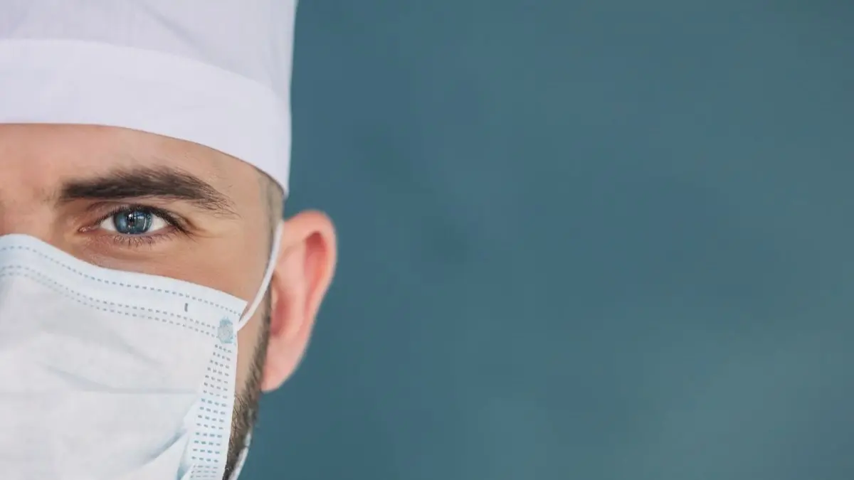 Nahaufnahme eines Chirurgen mit OP-Maske und Haube als Symbol fuer die Ambulantisierung in der medizinischen Versorgung