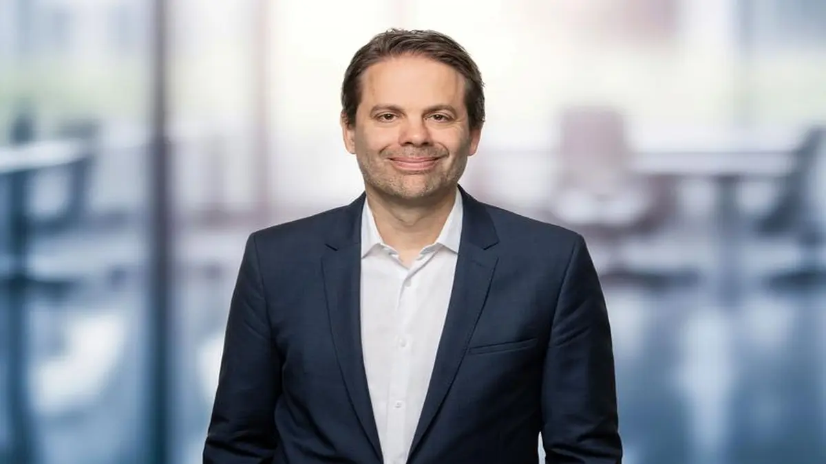 Professionelles Porträtfoto eines Mannes im dunkelblauen Sakko mit weißem Hemd vor unscharfem Büro-Hintergrund