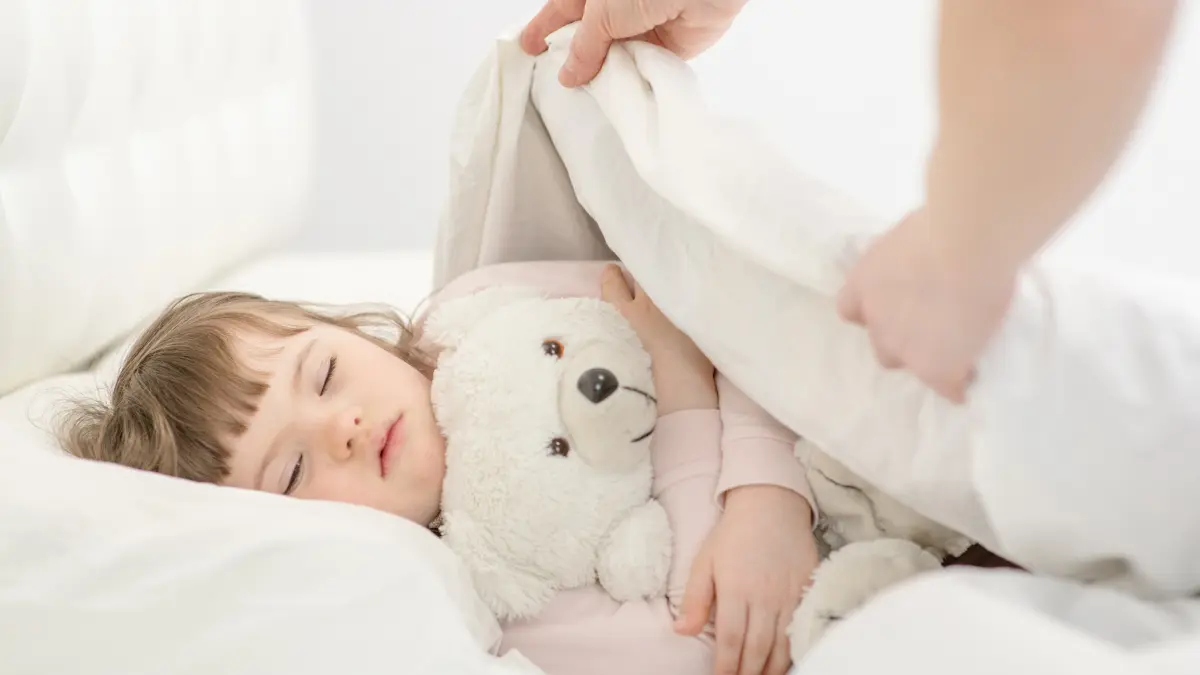 Kleines Mädchen mit Down-Syndrom schläft und wird von Mutter zugedeckt.