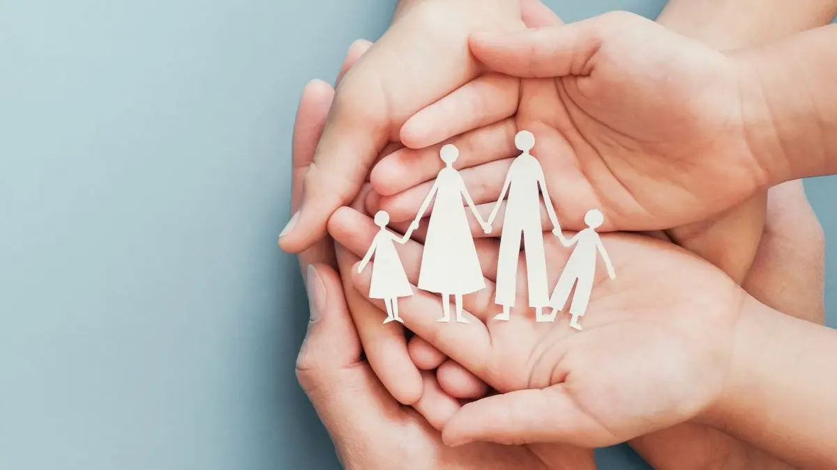 Haende halten schuetzend Papierfamilie als Symbol fuer familiaere Krankheitslast bei chronischer spontaner Urtikaria CSU