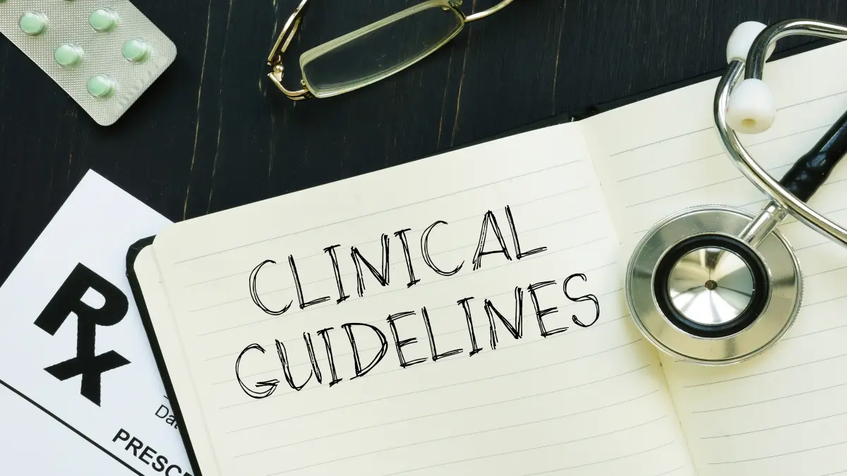 Notizbuch mit der Aufschrift „Clinical Guidelines“, Stethoskop, Brille und Medikamentenpackung – Symbolbild für medizinische Leitlinien und Therapieempfehlungen