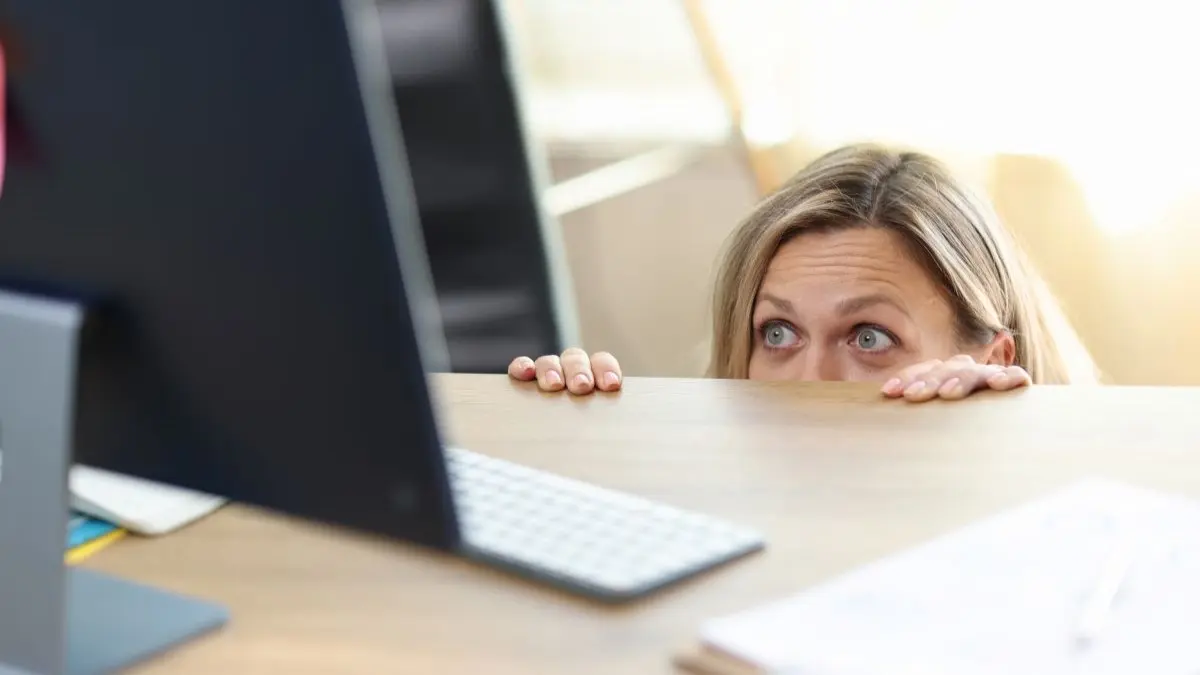 Frau lugt aengstlich ueber Schreibtischrand auf Computermonitor als Symbol fuer Morbus Google und Cyberchondri