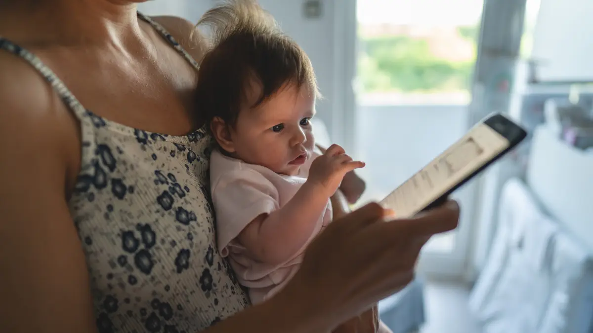 Mutter hält Säugling am Arm und tipp auf ihrem Smartphone