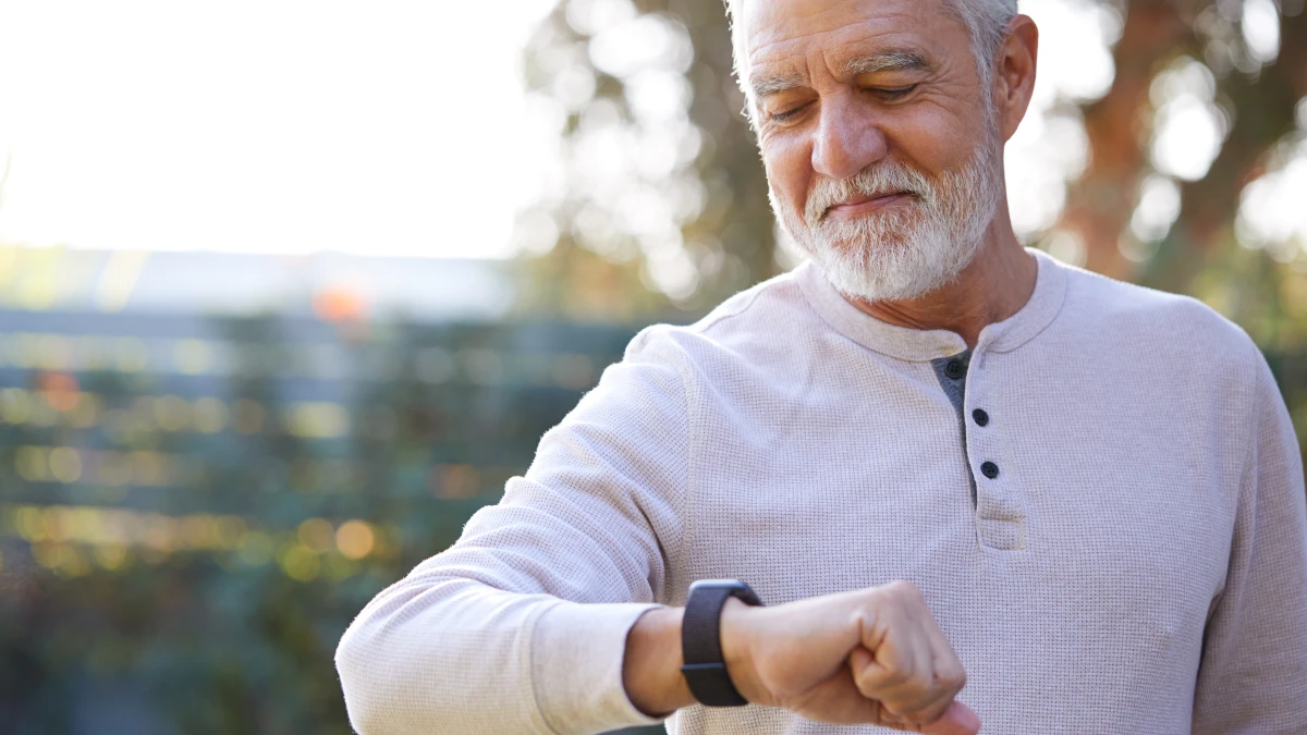 Ein älterer Mann schaut auf seine Smart Watch an seinem Handgelenk.