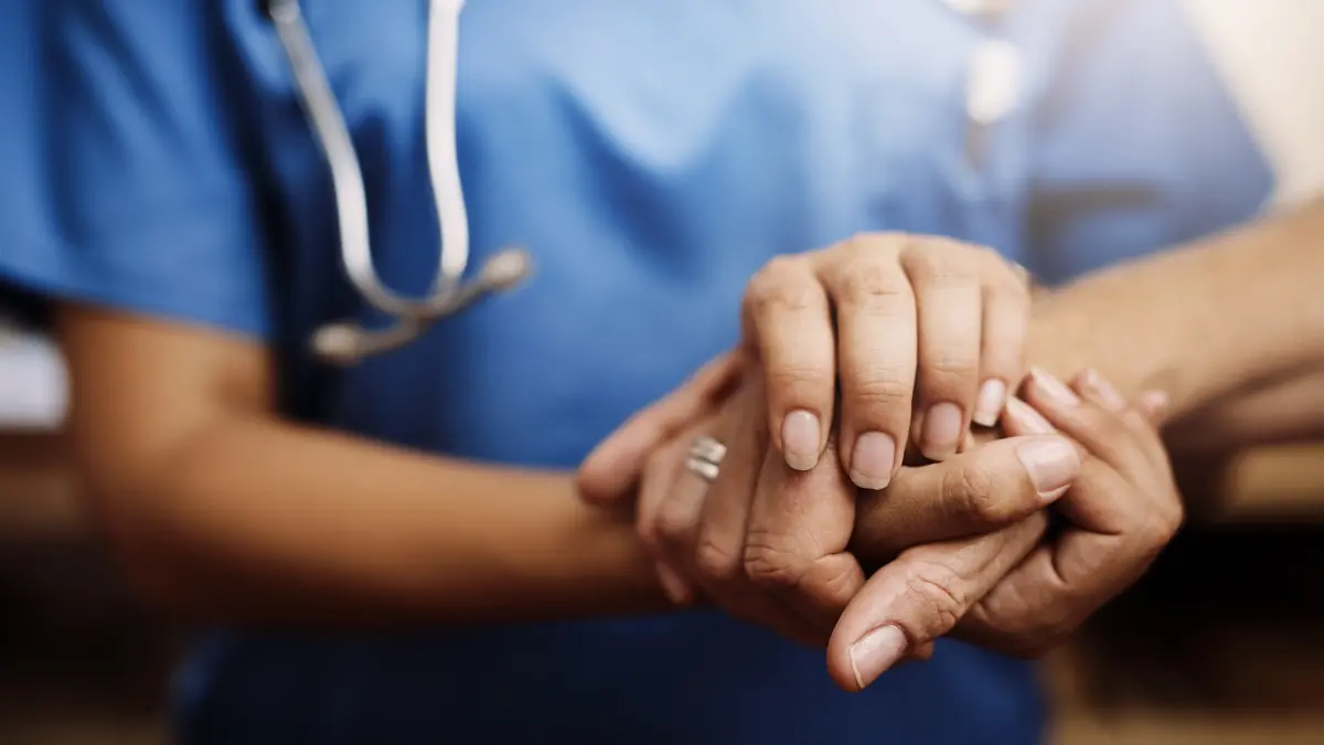 Pflegeperson hält tröstend die Hände eines Patienten – Symbolbild für Unterstützung bei der beruflichen Wiedereingliederung nach Krebs