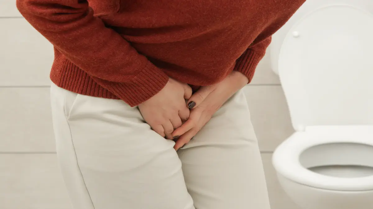 Person steht vor einer Toilette und hält sich den Unterleib – typisches Symbolbild für Harndrang oder Beschwerden beim Wasserlassen.