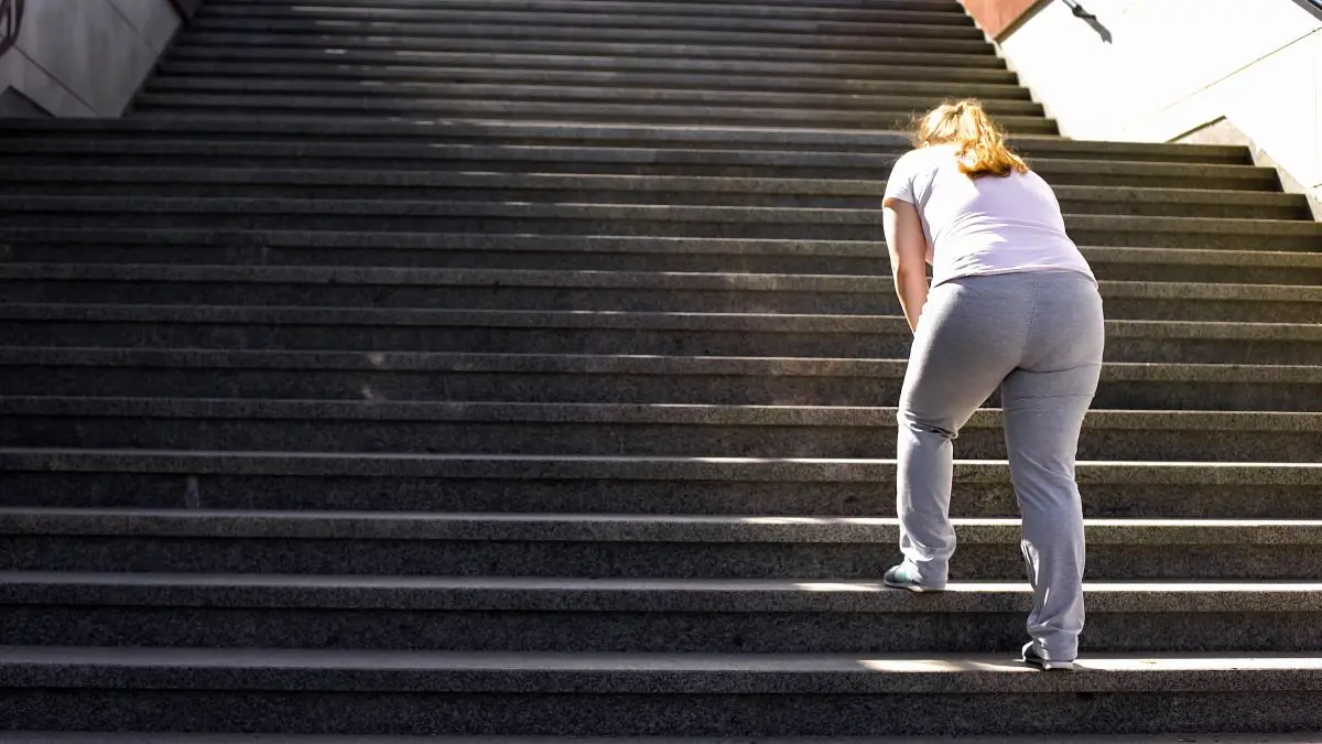 Frau mit Adipositas steigt mühsam eine Treppe hoch – Bewegung und Gesundheit bei Übergewicht.